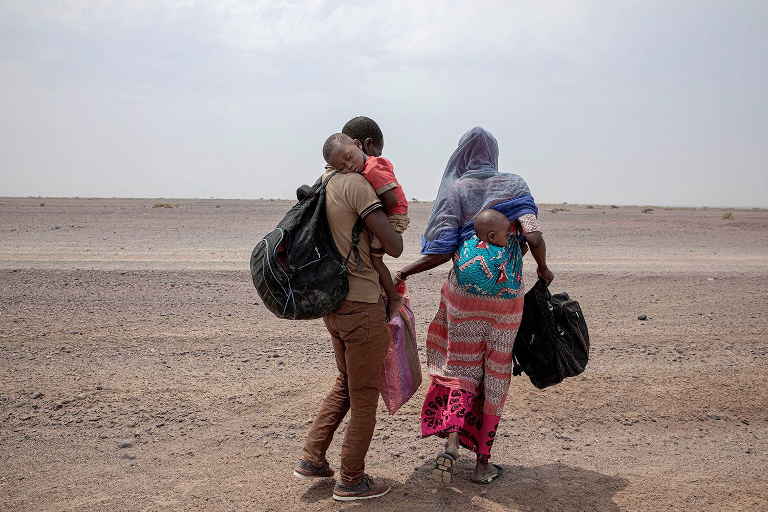 In this July 23, 2019 photo, Fatma and her husband Yacoub, migrants from Mali, carry their children as they make their way in Lahj, Yemen. Mohammed, traveled with her husband, a construction worker, and two children, through Djibouti on their way to Saudi. Once they reached the shore, they were held for several days by traffickers. Image by Nariman El-Mofty / AP Photo. Yemen, 2019.