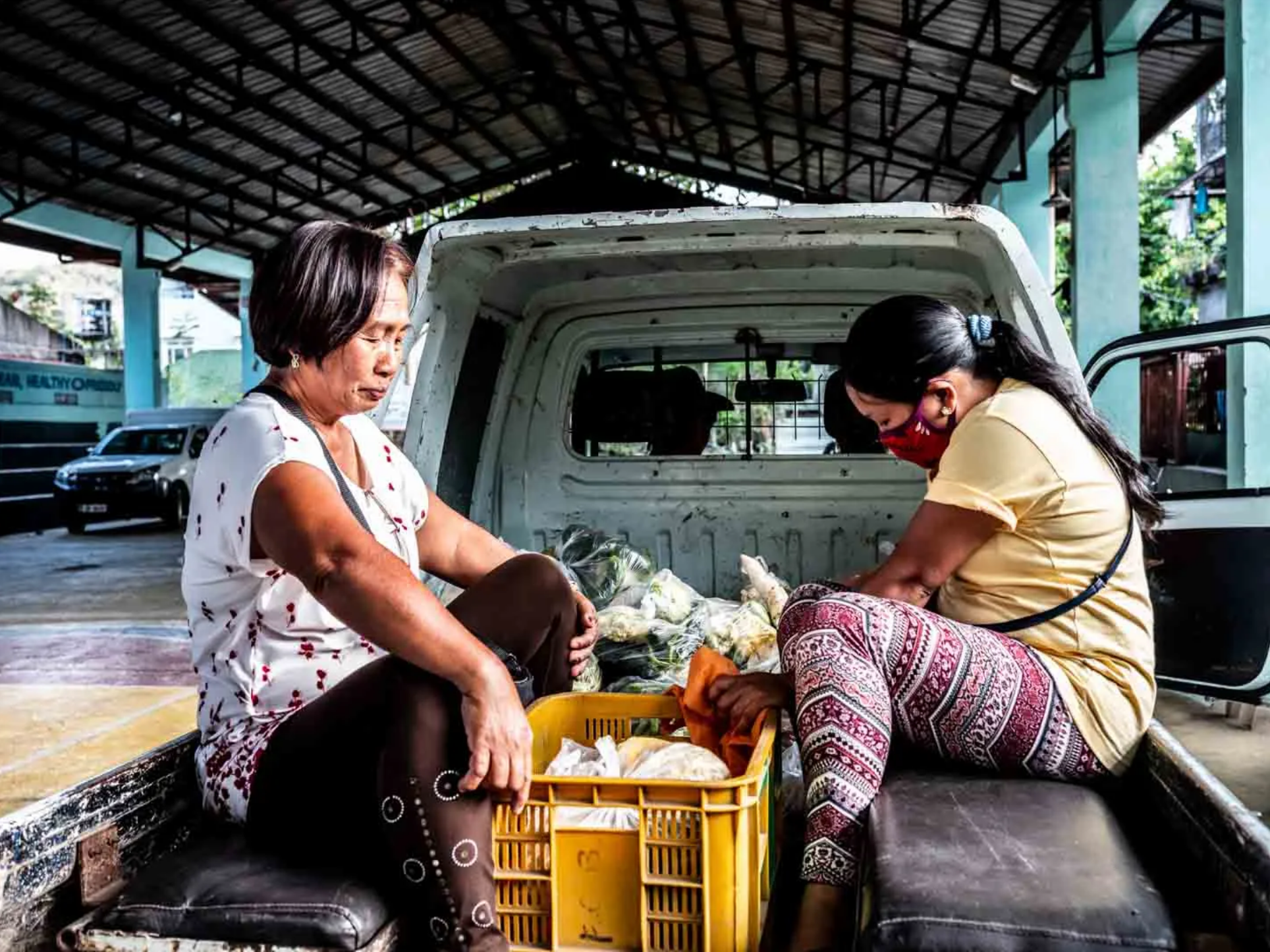 Reggie (left) sits at the back of a truck to distribute relief goods to the village. Image by Xyza Bacani. Philippines, 2020.