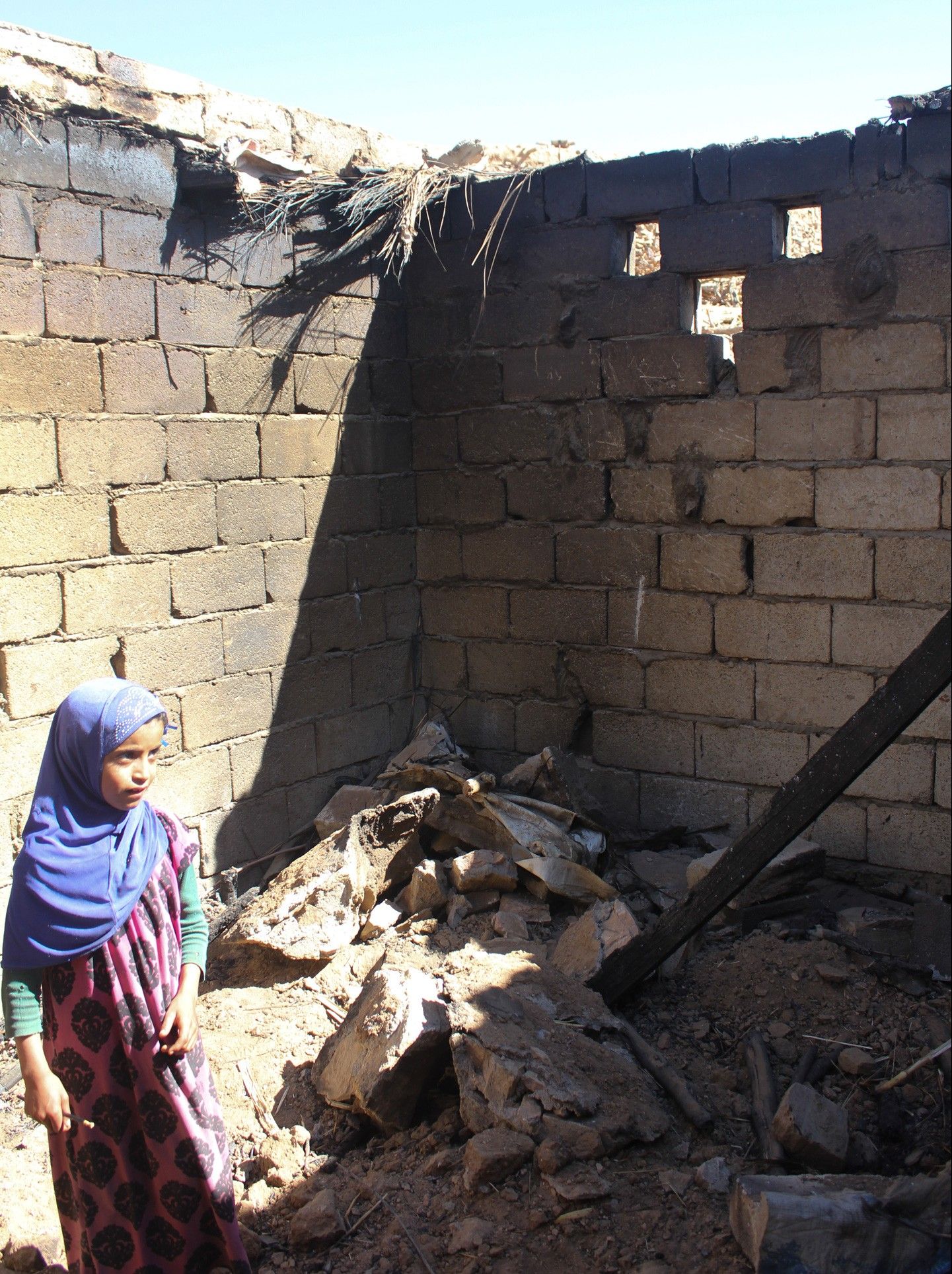 A girl stands in the burnt-out remains of a house destroyed during the U.S. Navy SEAL raid in the village of al Ghayil on January 29. Image by Iona Craig. Yemen, 2017.