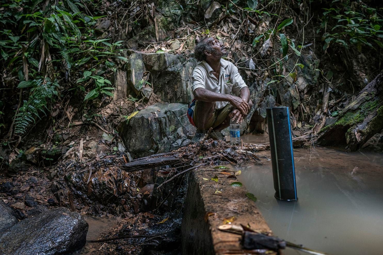 Johan Tahun takes a break atop the small concrete dam across the Tonduk River, built by the Malaysian government. Image by James Whitlow Delano. Malaysia, 2019.
