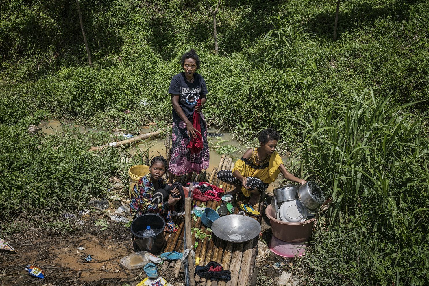 A mother and her two daughters wash pots and clothing at the water source that most Batek believe was contaminated by mining runoff. Despite that, they still use it as their primary water source. Image by James Whitlow Delano. Malaysia, 2019.