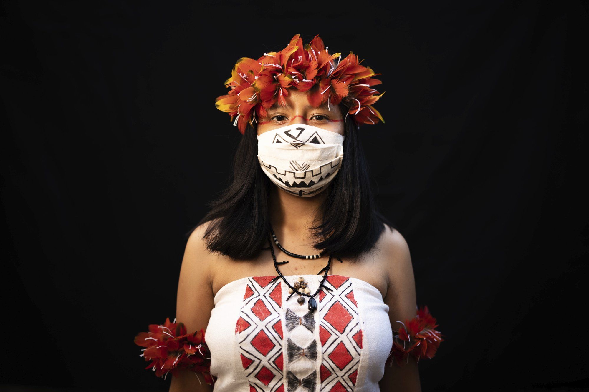 Yusuro Dupohtiro, 15, of the Dessana and Sateré Mawé indigenous ethnic groups, poses for a portrait wearing the traditional dress of her tribe and a face mask amid the spread of the new coronavirus in Manaus, Brazil, Wednesday, May 27, 2020. Image by Felipe Dana / AP Photo. Brazil, 2020.