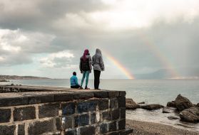 Blessing and two other teen-age Nigerian girls watch a rainbow over the short stretch of water separating Sicily from mainland Italy. Eighty percent of young Nigerian women who cross the Mediterranean are trafficked into sexual exploitation. Image by Ben Taub. Italy, 2017.
