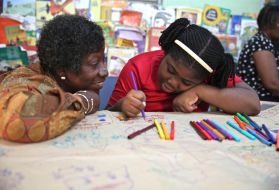 Dr. Claudette Crawford-Brown interacts with Shaniqua Long during an art therapy session at Shortwood Practising Infant, Primary and Junior High School in Kingston, Jamaica. Long's mother migrated to the United States. Image by Sabriya Simon. Jamaica. From Melissa Noel's Pulitzer Center-supported project, "Beyond The Barrels: How Migration Impacts Caribbean Children."