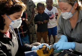 Tiziana Lembo (left) and Alison Peel take samples from bats while children watch in Morogoro, Tanzania. Image by Alexander Torrence. Tanzania.