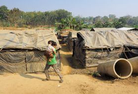 A boy carries another child in Kutapalong Refugee Camp. In this unofficial camp, tents are constructed with plastic tarps that had been used to evaporate seawater. Image by Doug Bock Clark. Bangladesh, 2017.